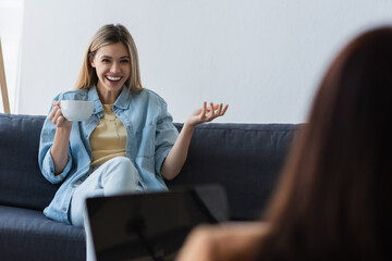 happy woman with cup of tea talking to psychologist on blurred foreground