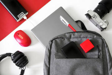 Laptop, smartphone, power bank, headphones, mouse, camera and backpack or bag on white and red...