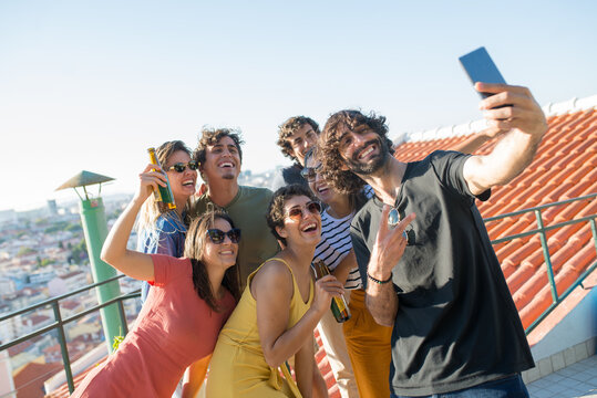Cheerful friends taking selfie at party. People of different nationalities holding brown bottles, smiling at camera. Taking pictures with phone. Party, friendship, social media concept