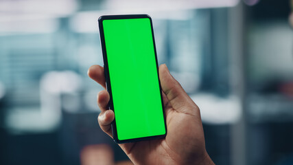 Black Businessman with Green Screen Chroma Key Smartphone in Office. African-American Businessperson using Internet, Social Media, Online Shopping with Mobile Phone Device. Over Shoulder
