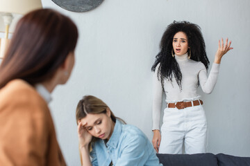 Naklejka premium african american lesbian woman quarreling near depressed girlfriend and blurred psychologist