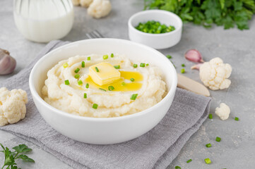 Cauliflower puree with butter and green onions in a white bowl on a gray concrete background. Healthy food. Copy space.