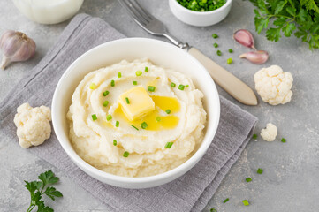 Cauliflower puree with butter and green onions in a white bowl on a gray concrete background. Healthy food. Copy space.
