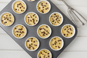 Raw dough for muffins with chocolate chips in baking form on a white wooden background. Recipe step by step. Top view.