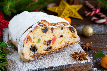 Christmas stollen with dried fruits and powdered sugar on a board on a dark wooden background. Copy space.