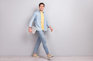 Photo of positive cheerful guy wear jeans shirt holding gadget empty space isolated concrete grey wall background