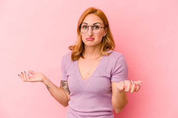 Young caucasian woman isolated on pink background doubting and shrugging shoulders in questioning...