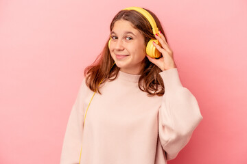 Little caucasian girl listening to music isolated on pink background trying to listening a gossip.