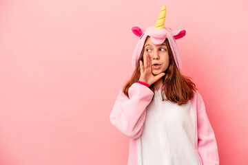 Little caucasian girl wearing a unicorn pajama isolated on pink background is saying a secret hot braking news and looking aside