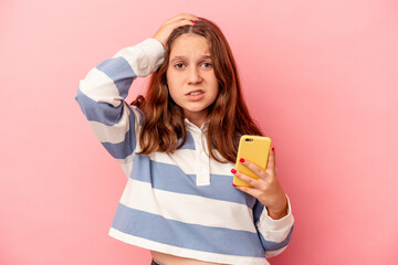 Little caucasian girl holding mobile phone isolated on pink background being shocked, she has...