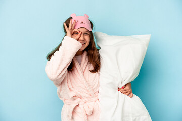 Little caucasian girl going to sleep isolated on blue background excited keeping ok gesture on eye.