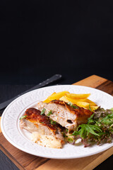Food concept Homemade Veal cordon bleu with salad and french fried in white ceramic plate on wooden board and black slate stone background with copy space