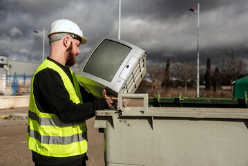 Trabajador del centro de reciclaje arrojando un viejo televisor de tubo en un contenedor de basura...