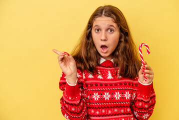 Little caucasian girl holding Christmas stick isolated on yellow background pointing to the side