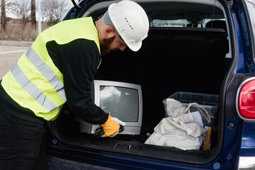 Trabajador de un centro de reciclaje sacando un viejo televisor de tubo del maletero de un coche....