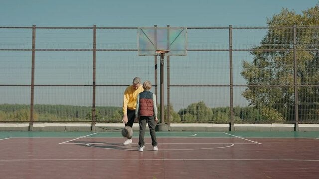 Father teaches son to get around in basketball on a court on a sunny day. Family exercises together. Man enjoying day at the park training with his son. High quality 4k footage