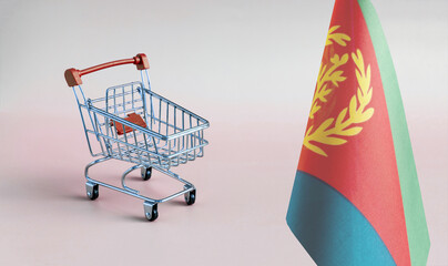 An empty metal shopping basket and the flag of the State of Eritrea on a light background is a...