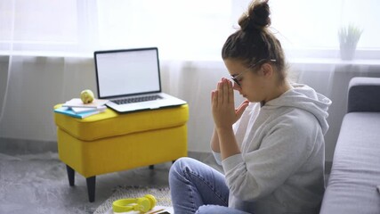 Woman in glasses meditates in yoga pose before laptop while takes break in distant work. Lady doing feels relieved and stress free, breathing exercise, mental balance concept 