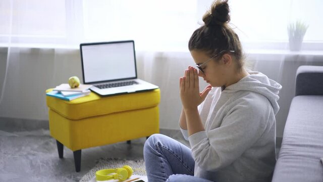 Woman in glasses meditates in yoga pose before laptop while takes break in distant work. Lady doing feels relieved and stress free, breathing exercise, mental balance concept 