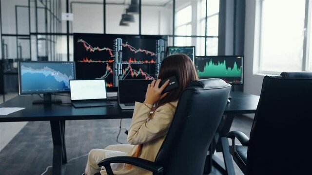 Excited woman talks by phone. Team of stockbrokers works together in modern office at daytime