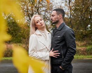 Portrait of young couple in love. Happy man and woman posing near the road. Woman looking to the camera. View through yellow leaves