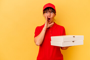 Young delivery woman holding pizzas isolated on yellow background is saying a secret hot braking news and looking aside