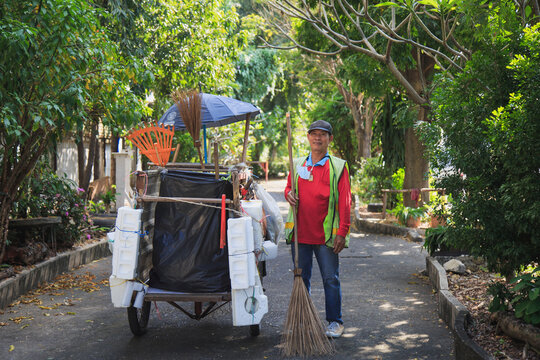 Portrait happy old Asian man street cleaner standing next to an old gabage cart before going to work with nature background.
