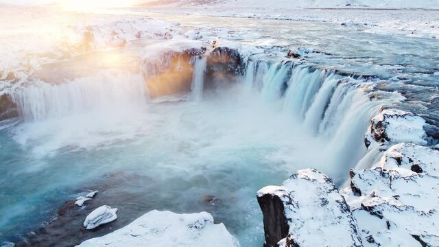 Flying near Godafoss Waterfall in the North of Iceland. Aerial shot of high water cascades shining at sunset. Blue waters splashing and foaming. Melting ice natural pattern.