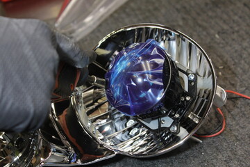 Car headlight in repair close-up. An auto mechanic wearing gloves installs the lens into the headlight housing. The concept of a car service.Installation of LED lenses in the headlight. LED lenses.