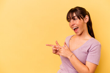 Young Argentinian woman isolated on yellow background points with thumb finger away, laughing and carefree.