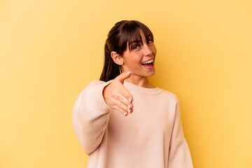 Young Argentinian woman isolated on yellow background stretching hand at camera in greeting gesture.