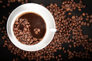Cup of aromatic coffee with coffee beans on a dark background