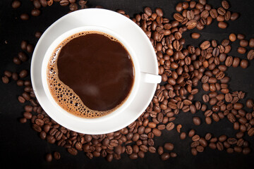 Cup of aromatic coffee with coffee beans on a dark background