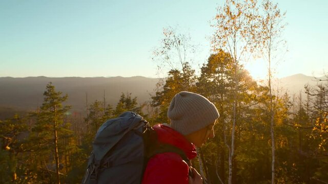 slow motion young confident woman in red jacket and beanie. girl walks, enjoying nature and looking confident and happy with her hiking expedition outdoors on top of mountain at sunset.