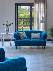 Fototapeta na wymiar Blue classic sofa in front of the window, carpet design, white table vase of plant, lamp, garden background.