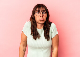 Young Argentinian woman isolated on pink background shrugs shoulders and open eyes confused.