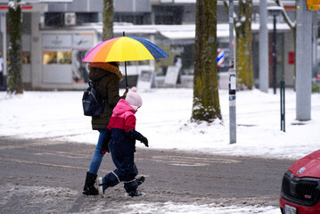 Mother and daughter walking on street on a snowy winter day at Schwamendingen Square at City of Zürich. Photo taken December 10th, 2021, Zurich, Switzerland.