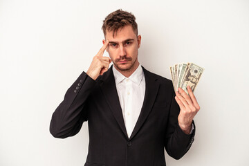 Young caucasian business man holding bank notes isolated on white background pointing temple with finger, thinking, focused on a task.