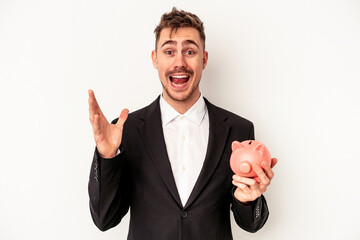 Young caucasian business man holding piggy bank isolated on white background receiving a pleasant...