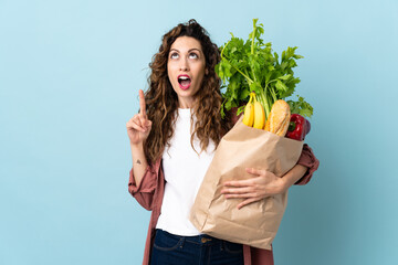 Young woman holding a grocery shopping bag isolated on blue background thinking an idea pointing the finger up