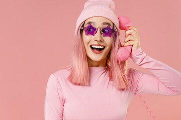 Young fun woman with bright dyed rose hair in rosy top shirt hat glasses hold handset vintage phone...