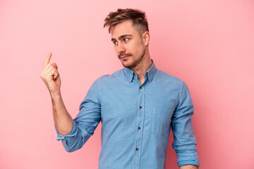 Young caucasian man isolated on pink background pointing with finger at you as if inviting come closer.