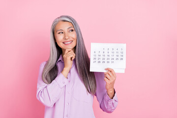 Portrait of attractive minded cheerful gray-haired woman holding calendar thinking isolated over...