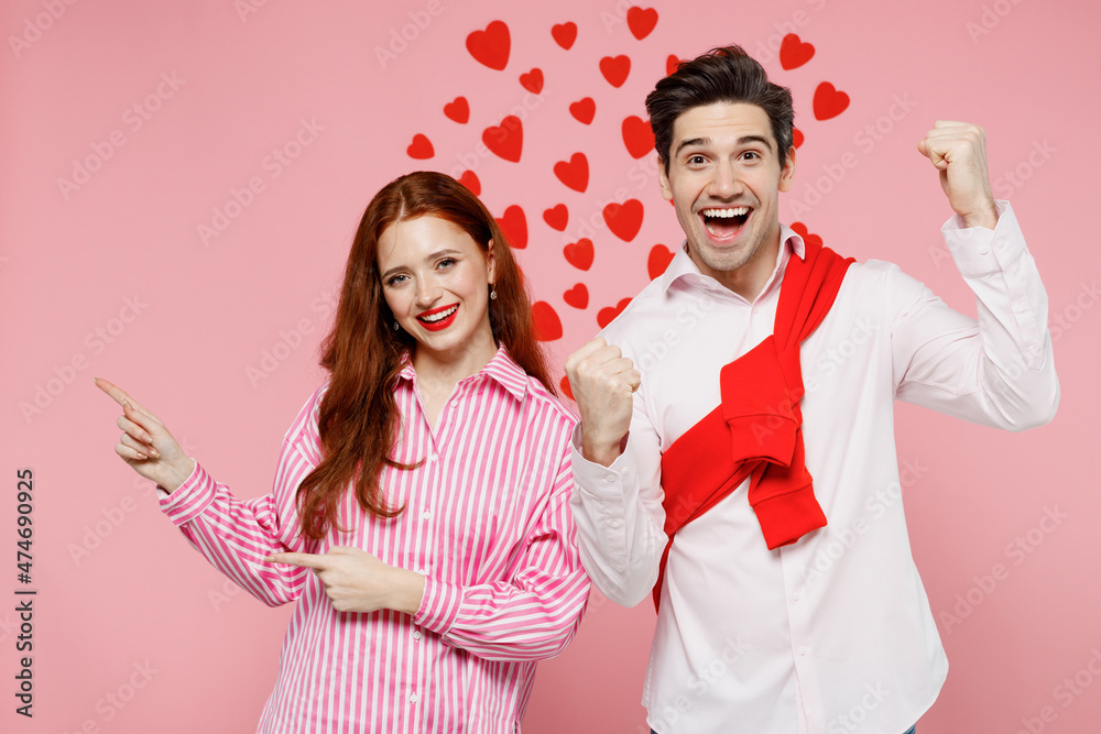 Poster Young couple two friends woman man 20s in casual shirt point index finger aside on copy space area do winner gesture isolated on plain pink background. Valentine's Day birthday holiday party concept