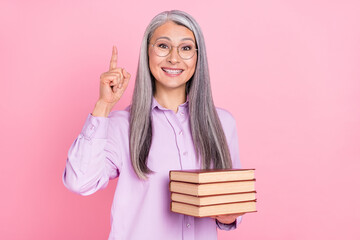 Portrait of attractive cheerful gray-haired woman holding books pointing up find solution isolated...