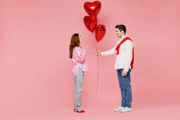 Full body side view young couple two friend woman man 20s in shirt hold bunch of red inflatable balloons isolated on plain pastel pink background studio Valentine's Day birthday holiday party concept