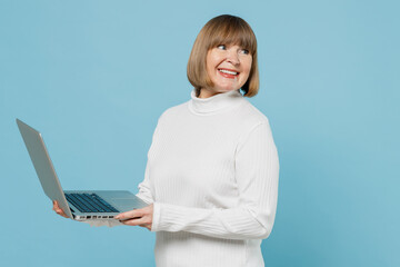 Elderly copywriter woman 50s wear white knitted sweater hold use work on laptop pc computer look...