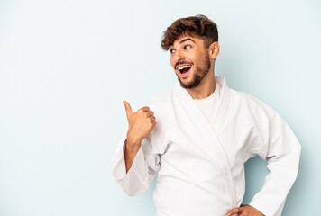 Young mixed race man doing karate isolated on blue background points with thumb finger away, laughing and carefree.