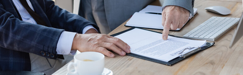 cropped view of senior businessman pointing at contract near colleague, banner
