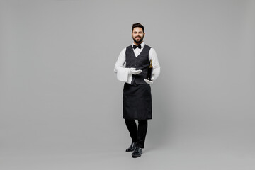 Full size young barista male waiter butler man 20s wear white shirt vest elegant uniform work at cafe hold bottle of wine isolated on plain grey background studio portrait Restaurant employee concept